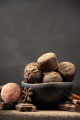 Close-up of chocolates with cocoa powder in dark bowl on wooden table with cinnamon and anise, selective focus, gray background, vertical, with copy space