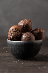 Close up of chocolates in dark bowl on wooden table, selective focus, gray background, vertical,...