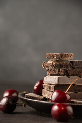 View of stack of chocolate bars in plate on wooden table with cherries, selective focus, gray background, vertical, with copy space