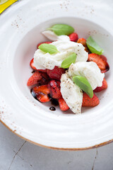 Beige plate with torn mozzarella cheese, balsamic strawberries and fresh green basil, vertical shot, closeup, selective focus