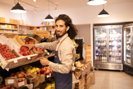 Ethnic smiling man choosing ripe tomatoes in supermarket