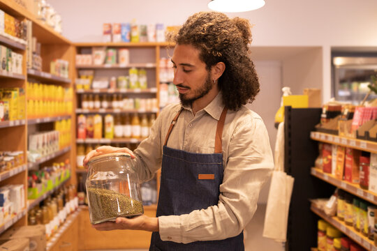 Ethnic male worker with jar of bulk standing in supermarket