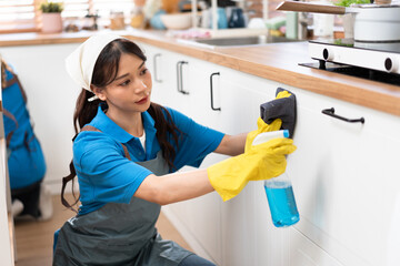 Asia woman in workwear maid cleaning home holding bottle spray and wiping with microfiber cloth in...