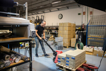 Strong middle aged man pulling material on pallet jack in factory