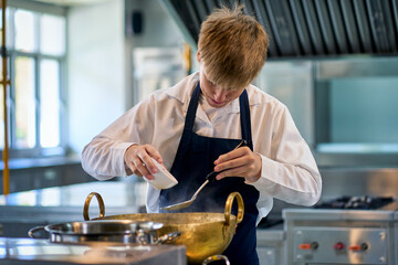 Single young boy in chef uniform try to cooking food with brass pot in kitchen for make a soup menu.
