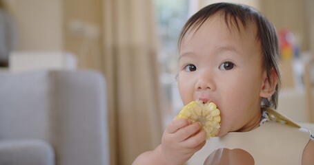 Happy Cute Adorable Little Asian Toddler Girl Enjoying Eating fresh vegetable Corn Having Fun and smiling at Home, Joyful BLW Mealtimes for Healthy Nutrition