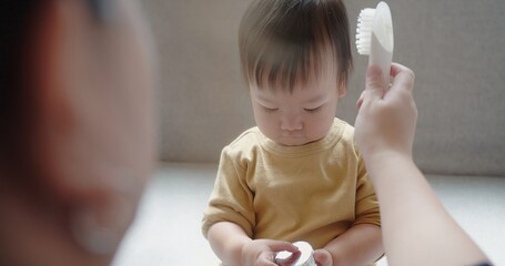 Happy Asian family mother tenderly comb hair make hairstyle of her baby, little daughter child...