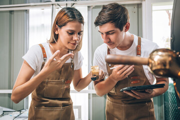 Young Adult Small Business Owner's Caucasian Couple Working Together in Coffee Roaster Factory, Professional Barista Checking the Quality and Aroma After Roasted with Machine in Warehouse.