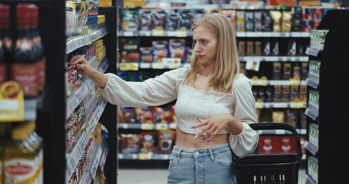 inflated prices buyer takes product from the shelf in search of the right one grocery department and is horrified by the price. Wide-eyed female immediately return product on the shelf inflated prices