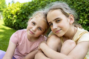 Two girls sisters of school age hug each other. A walk through the summer city park. Love and friendship within the family