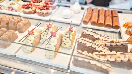 A variety of cakes covered with chocolate and decorated with pistachio mousse. A showcase in a pastry shop with delicious desserts with fresh berries and cream. Delicious pastries in the coffee shop.