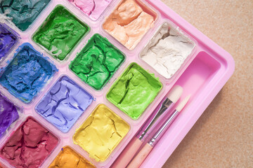 Dried colorful gouache in pink painting palette box with two pieces of white paint brush. Cracked water color and small brush.