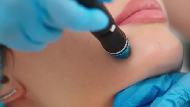 Cosmetology clinic. Professional female cosmetologist doing hydrafacial procedure while being a work. Attractive nice woman lying on the medical bed while having beauty procedures