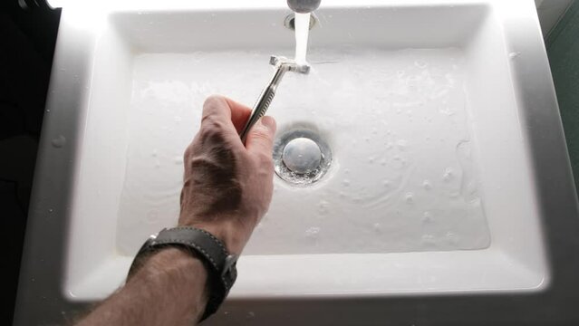 Cleaning shaving razor in bathroom sink. Rinsing off razor with water.