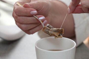 woman's hand squeezes out a bag of tea - obrazy, fototapety, plakaty