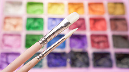 Close-up photo of  two pieces white paint brush with dried colorful gouache in pink painting palette box bokeh backgrounds.  Small brush and cracked water color