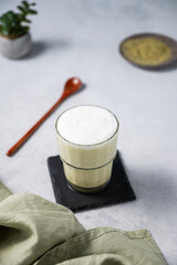 Matcha latte with ice. Green tea with milk in a glass on a light background with spoon, napkin. The concept of a traditional healthy Japanese summer refreshing drink.