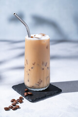 Iced coffee latte in a tall glass with milk on a light background with coffee beans and morning...