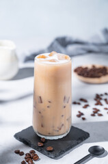 Iced coffee latte in a tall glass with milk on a blue background with coffee beans and morning shadows. Summer refreshment concept.