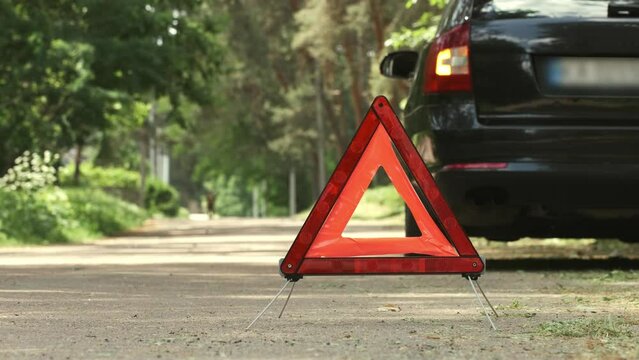 Red triangle, red emergency stop sign and black car with turned on blinkers. Emergency stop of the car with technical problems on the road. Safety procedure while having a vehicle broken down