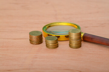 A magnifying glass placed upon a bed of coins, symbolizing financial development, banking accounts, statistical analysis, investment research, and stock exchange trading.