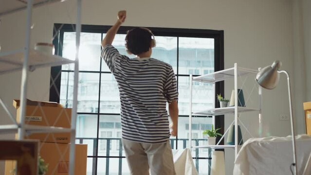greeting happiness joyful asian adult male wearing casual cloth and wirreless headphone dance music lover while unpack stuff relax from home moving house relocation ,he is happy to move in new house