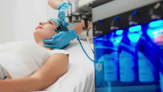 Cosmetology clinic. Professional female cosmetologist doing hydrafacial procedure while being a work. Attractive nice woman lying on the medical bed while having beauty procedures