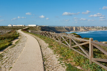 Fototapeta na wymiar View of the Sagres Fortress and Sagres village in Portugal. Wooden fence and walkway in the foreground