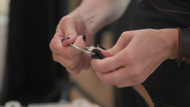 Medium close up of hands of craftswoman creating leather belt with eyelets for client in workshop