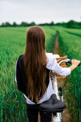 A girl on a bicycle with a basket in the middle of a wheat field