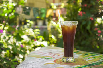 Iced Americano or Long Black Coffee in a long glass with a straw on a wooden table against a bright...