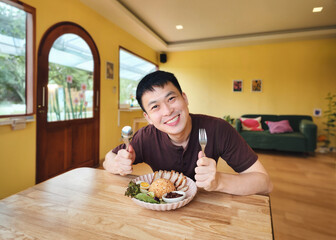 Asian man smiling and holding spoon and fork with crispy pork with rice in lunch
