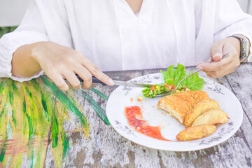 A woman wearing white clothes is slicing steak on a ceramic plate on a wooden table. Fried chicken steak served with tomato sauce and mixed vegetables. Concept for healthy food, fat loss, weight loss.
