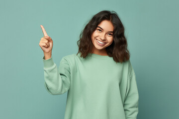 Excited young ginger teenager girl smiling and pointing index finger up at copy space expressing wow emotion standing isolated on green background studio copy space, advertisement concept. High - Powered by Adobe