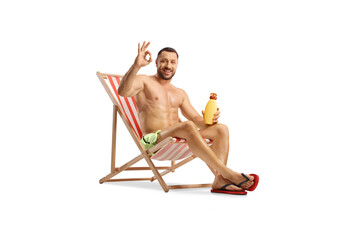 Fototapeta na wymiar Young man sitting on a beach chair holding a bottle of sunscreen and gesturing ok sign