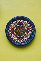 Assiette décorative en céramique colorée posée sur un mur jaune