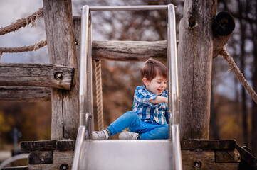 Little toddler boy in blue shirt wanted to slide down the metal slide