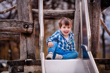 Little toddler boy in blue shirt trying to climb down a wooden ladder on playground