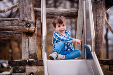 Little toddler boy in blue shirt trying to climb down a wooden ladder on playground