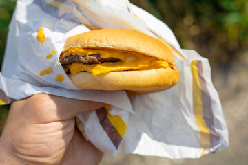 The concept of fast food and takeaway food. Big juicy burger with cheese in the hand