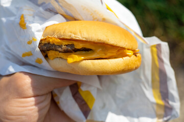 The concept of fast food and takeaway food. Big juicy burger with cheese in the hand
