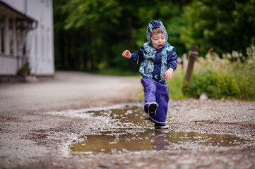 Little toddler boy in waterproof wearing playing in puddle with water