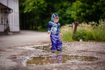 Little toddler boy in waterproof wearing playing in puddle with water