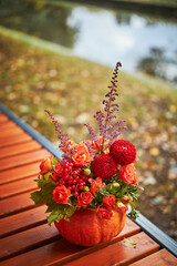 Beautiful bouquet of autumn flowers in pumpkin on bench outdoors. Beautiful floral decor for thanksgiving and halloween. Fall decor.