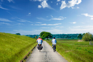 Two cyclists from behind on the Elbe cycle path next to the dyke. - obrazy, fototapety, plakaty