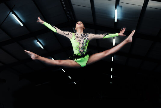 Woman, jump and gymnastics with fitness and competition, action and body with performance in arena. Female gymnast in air, athlete exercise with flexibility and health for sports, flying and acrobat