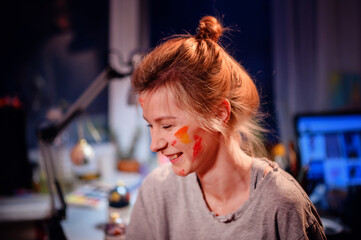 Portrait of young blonde woman in grey t-shirt with paint on face. Artist in working process