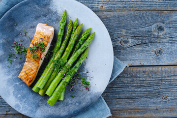 Traditional glazed green asparagus with salmon fillet and herbs served as top view on a design...