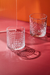 Two empty glass glasses on colored backgrounds with shadows from sunlight