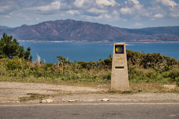 Stone monolith that marks the direction to follow for the road to Santiago, with arrow and shell, with the ocean in the background. Concept pilgrim, way, religion, travel.